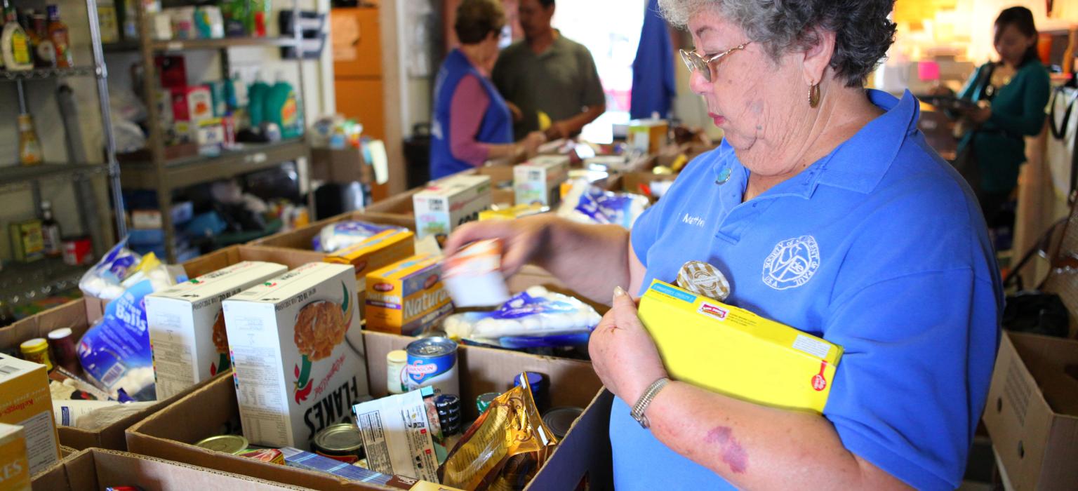 Food bank and Community Pantries Header Woman putting cans of food into a box