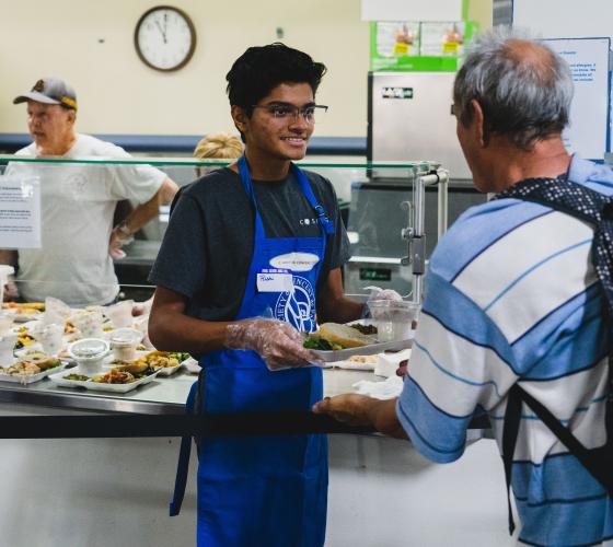 Dining Rooms VSO Header Young man handing a tray of food to an older man